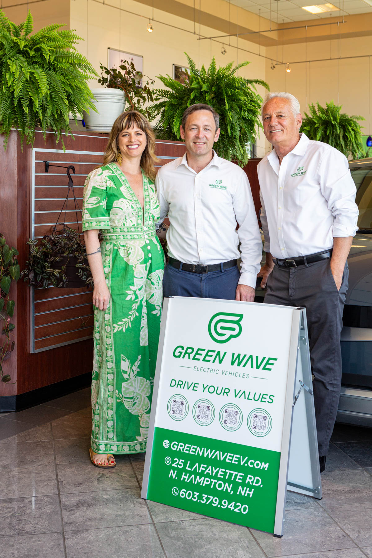 Три человека стоят рядом с вывеской Green Wave Electric Vehicles в автосалоне.